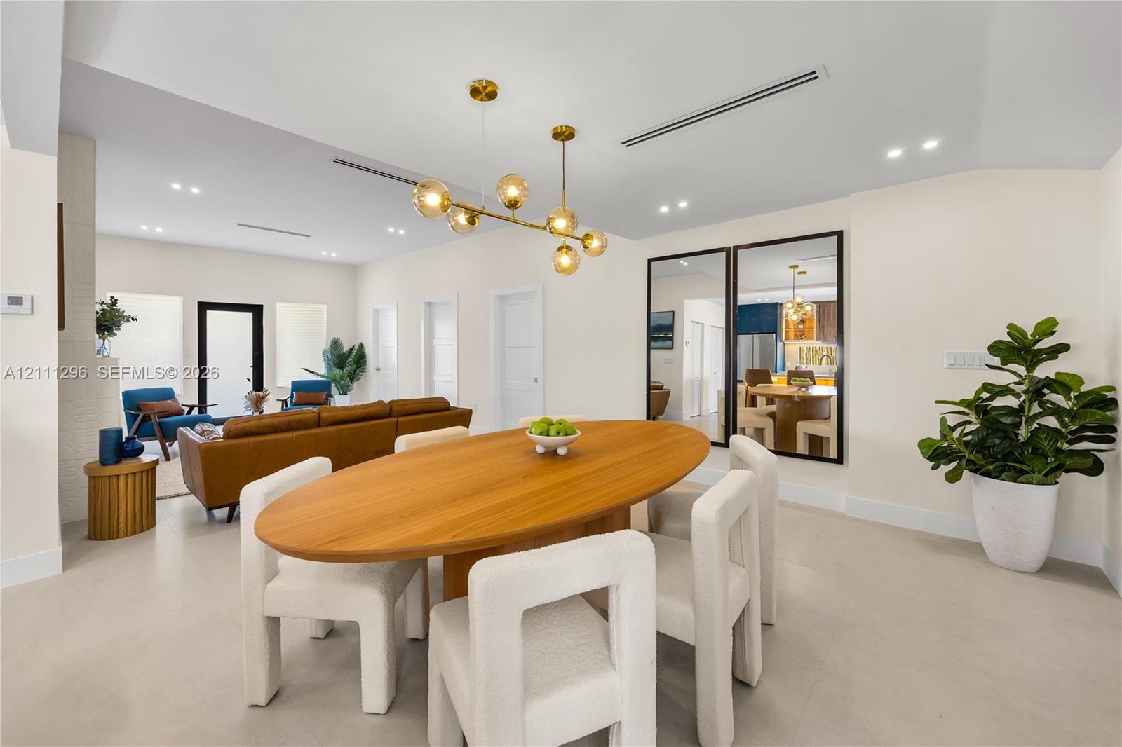 Open-concept interior featuring light-toned tile flooring, recessed linear lighting, a multi-arm brass finish chandelier, and large-scale floor-to-ceiling mirrors