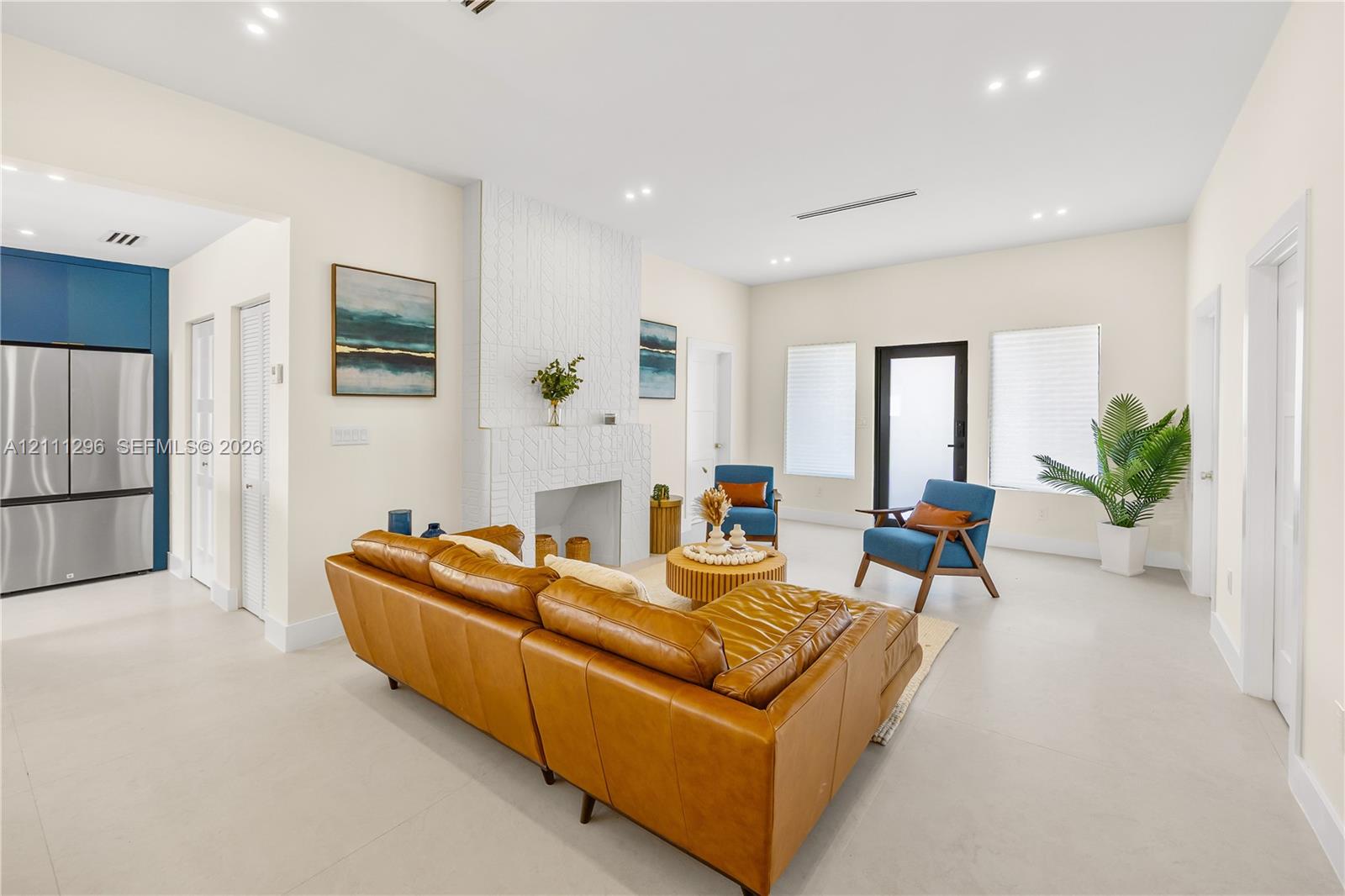 Living area featuring large-format tile flooring, recessed ceiling lighting, a textured floor-to-ceiling fireplace surround, and a glass-paneled exterior door