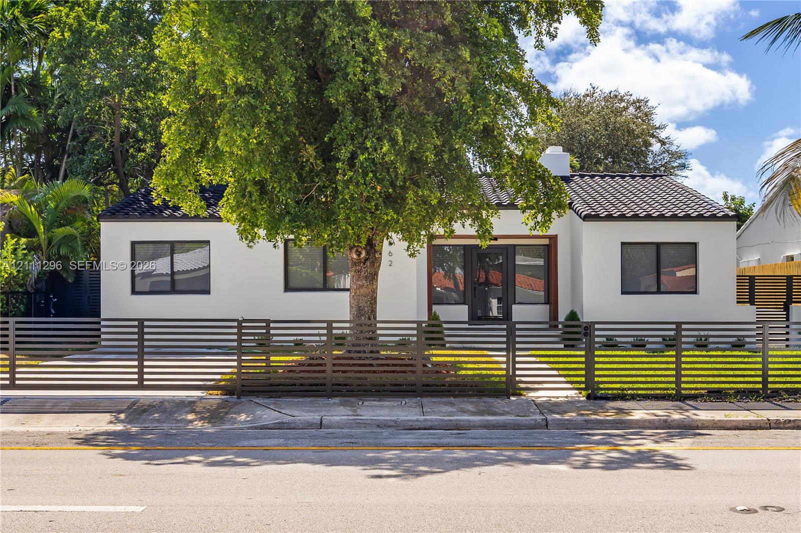 Single-story stucco exterior featuring a dark tile roof, horizontal slat metal fencing, and dark-framed windows