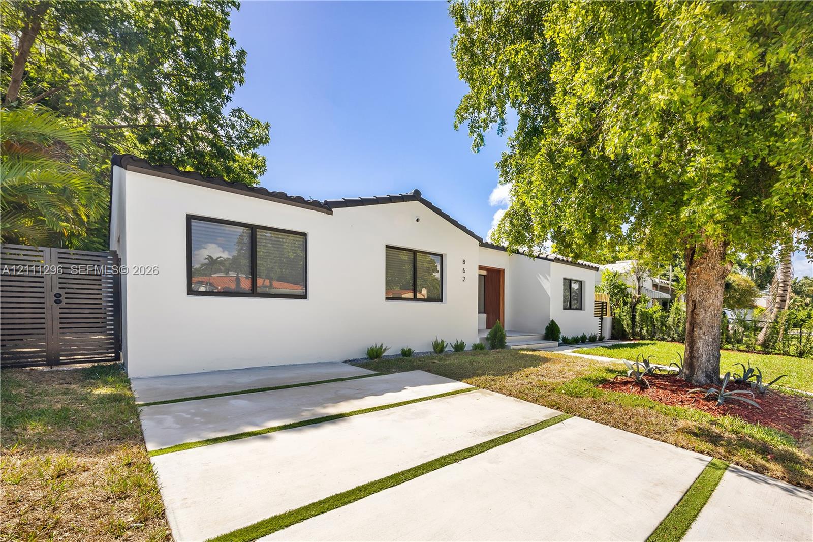 Stucco exterior featuring dark-framed windows, a concrete ribbon driveway with turf accents, and a horizontal slat privacy gate