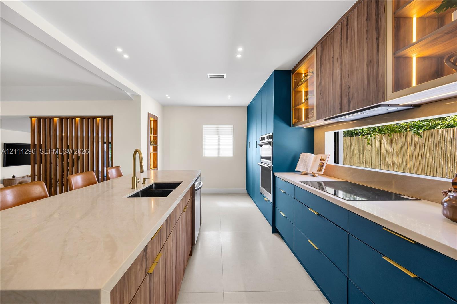 Modern kitchen featuring custom blue cabinetry, wood-finish lower cabinetry, stone-surface countertops, integrated under-cabinet lighting, and built-in double wall ovens