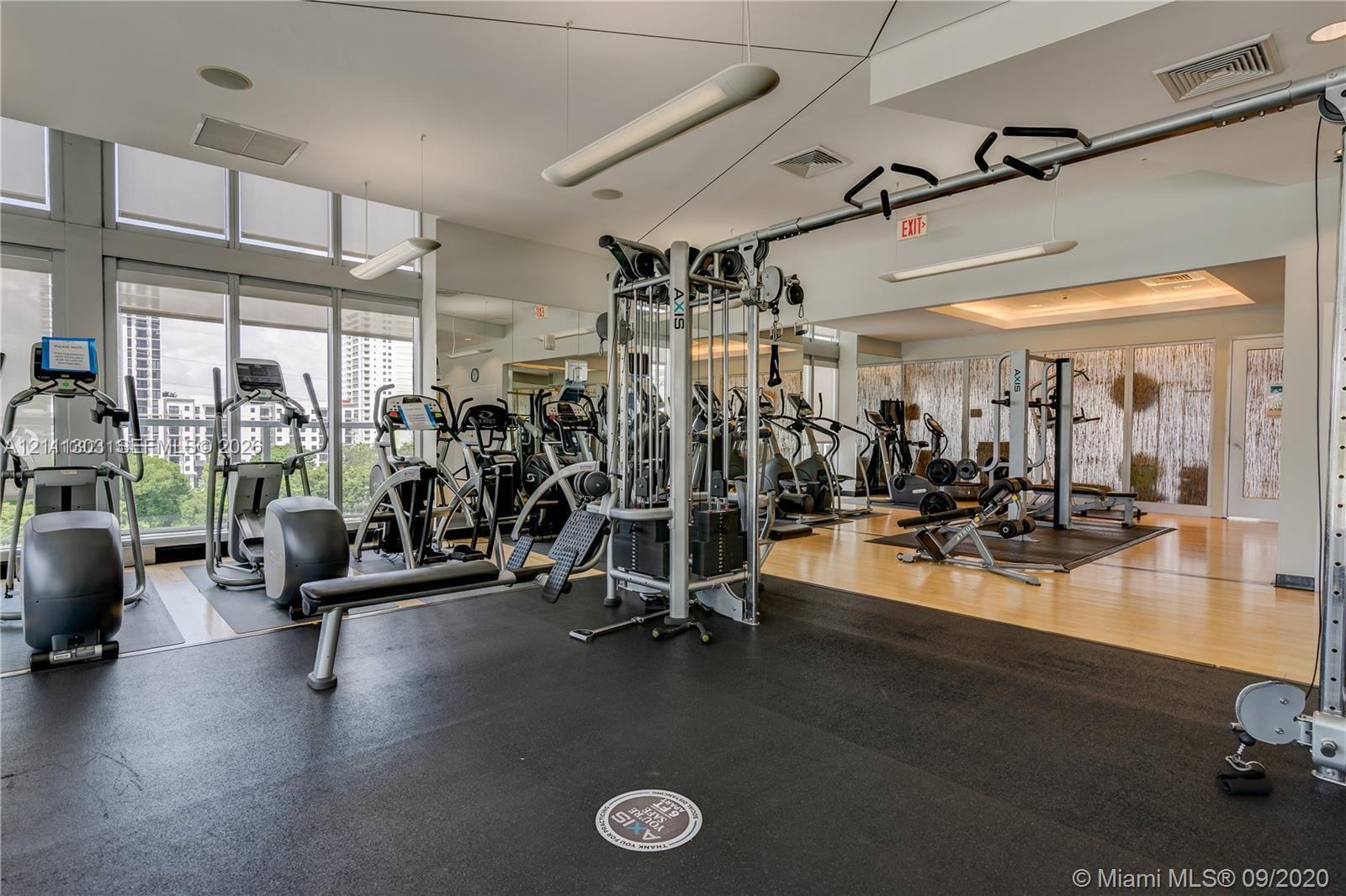 Fitness center featuring wall-to-wall mirrors, floor-to-ceiling windows, suspended linear lighting, and durable rubberized flooring