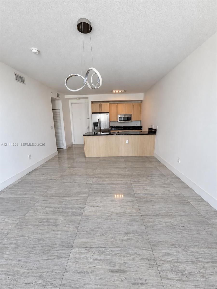 Large-format tile flooring, flat-panel light-finish cabinetry, dark solid-surface countertops, and contemporary circular chandelier lighting Large-format tile flooring, flat-panel light-finish cabinetry, dark solid-surface countertops, and contemporary circular chandelier lighting