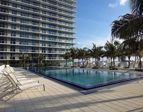 Infinity-edge swimming pool featuring a tiled waterline, surrounded by a paved deck with mature palm trees and a multi-story glass balcony exterior Infinity-edge swimming pool featuring a tiled waterline, surrounded by a paved deck with mature palm trees and a multi-story glass balcony exterior