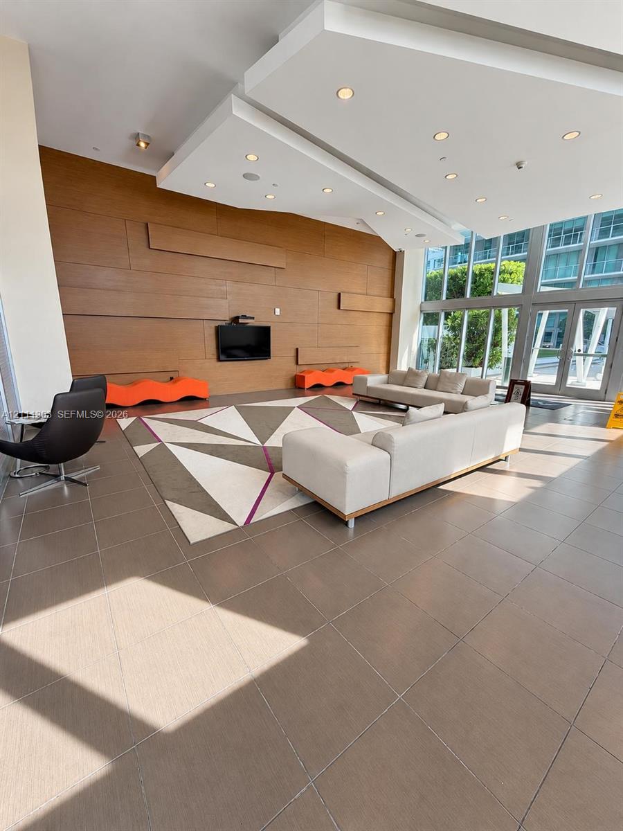Lobby area featuring wood-panel accent wall, tile flooring, recessed ceiling lighting, and floor-to-ceiling glass windows