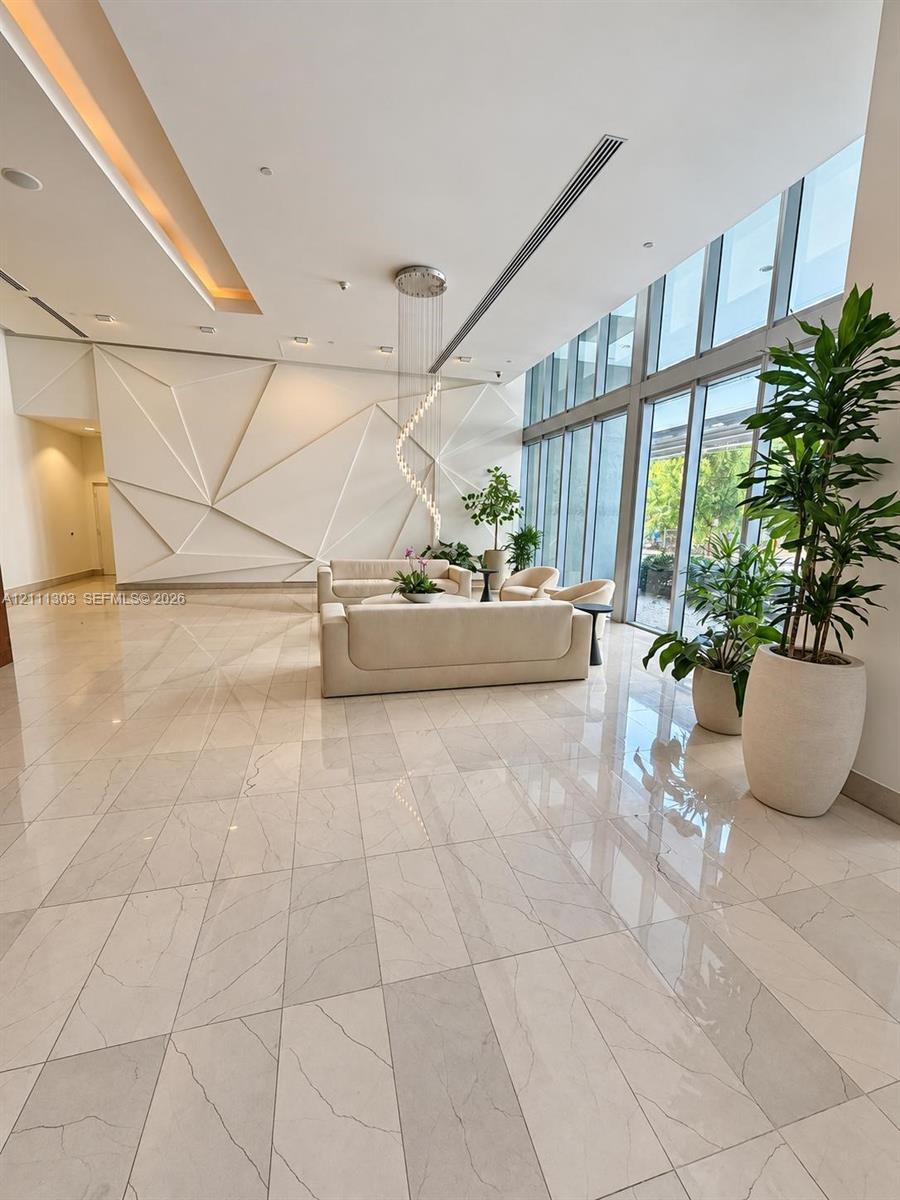 Grand entrance lobby featuring expansive floor-to-ceiling windows, polished stone tile flooring, a custom geometric accent wall, recessed architectural lighting, and a sculptural hanging pendant light