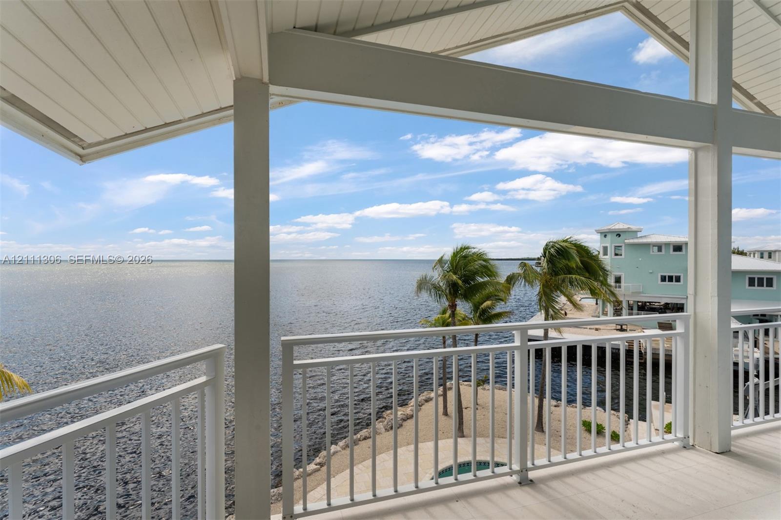 Covered balcony featuring vaulted tongue-and-groove ceiling, white metal railings, and direct water frontage