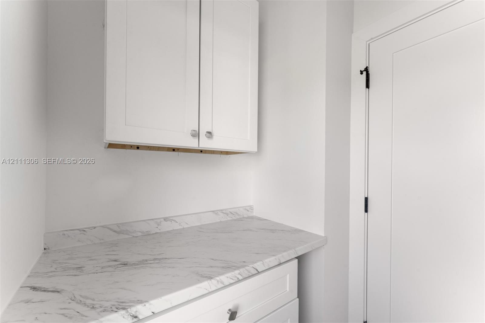 Shaker-style white cabinetry, stone-finish countertop with matching backsplash, and solid-core door with matte black hardware