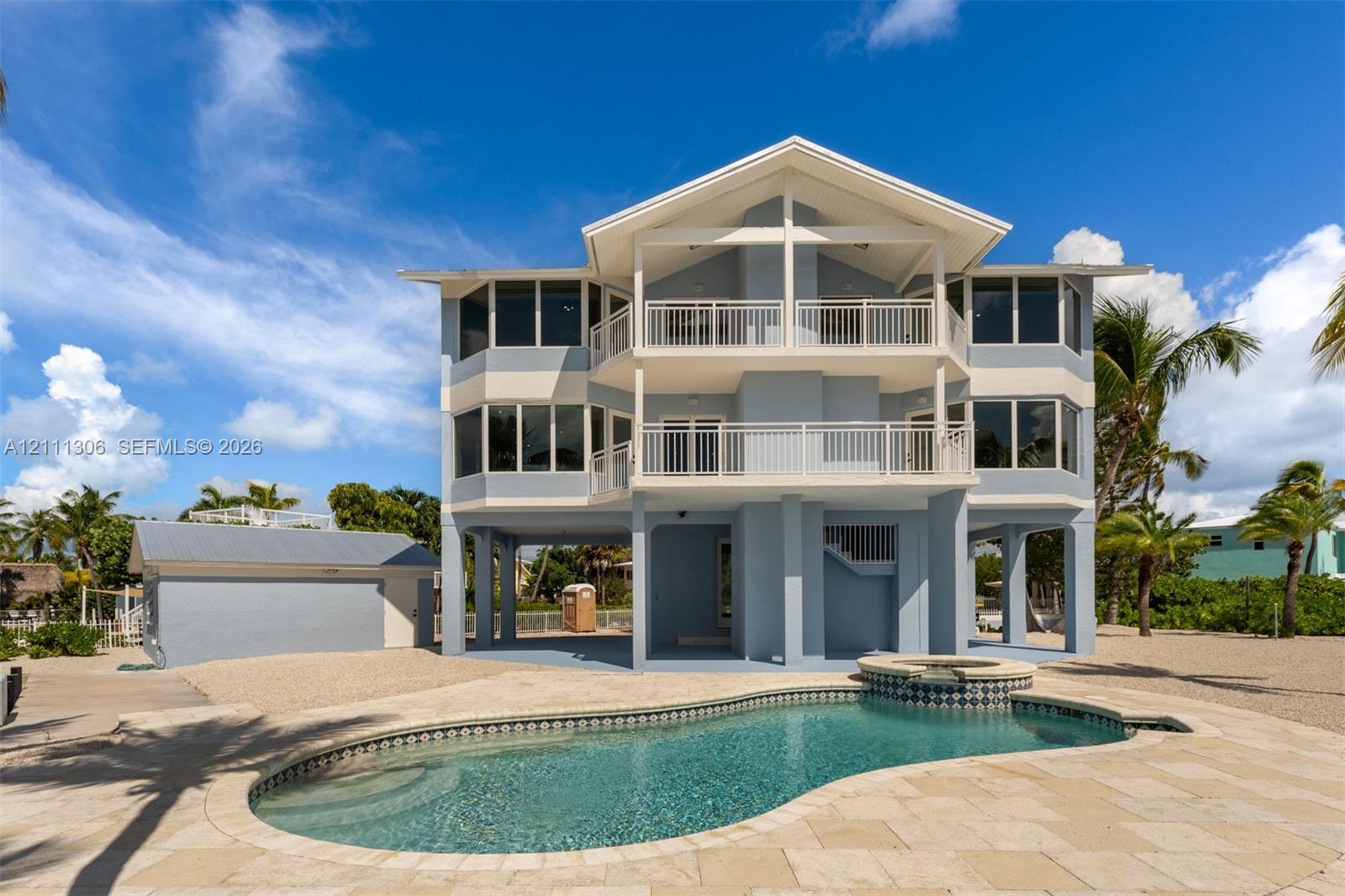 Multi-story exterior featuring double stacked balconies with white railings, a light-colored stone patio, and an inground swimming pool with a spillover spa
