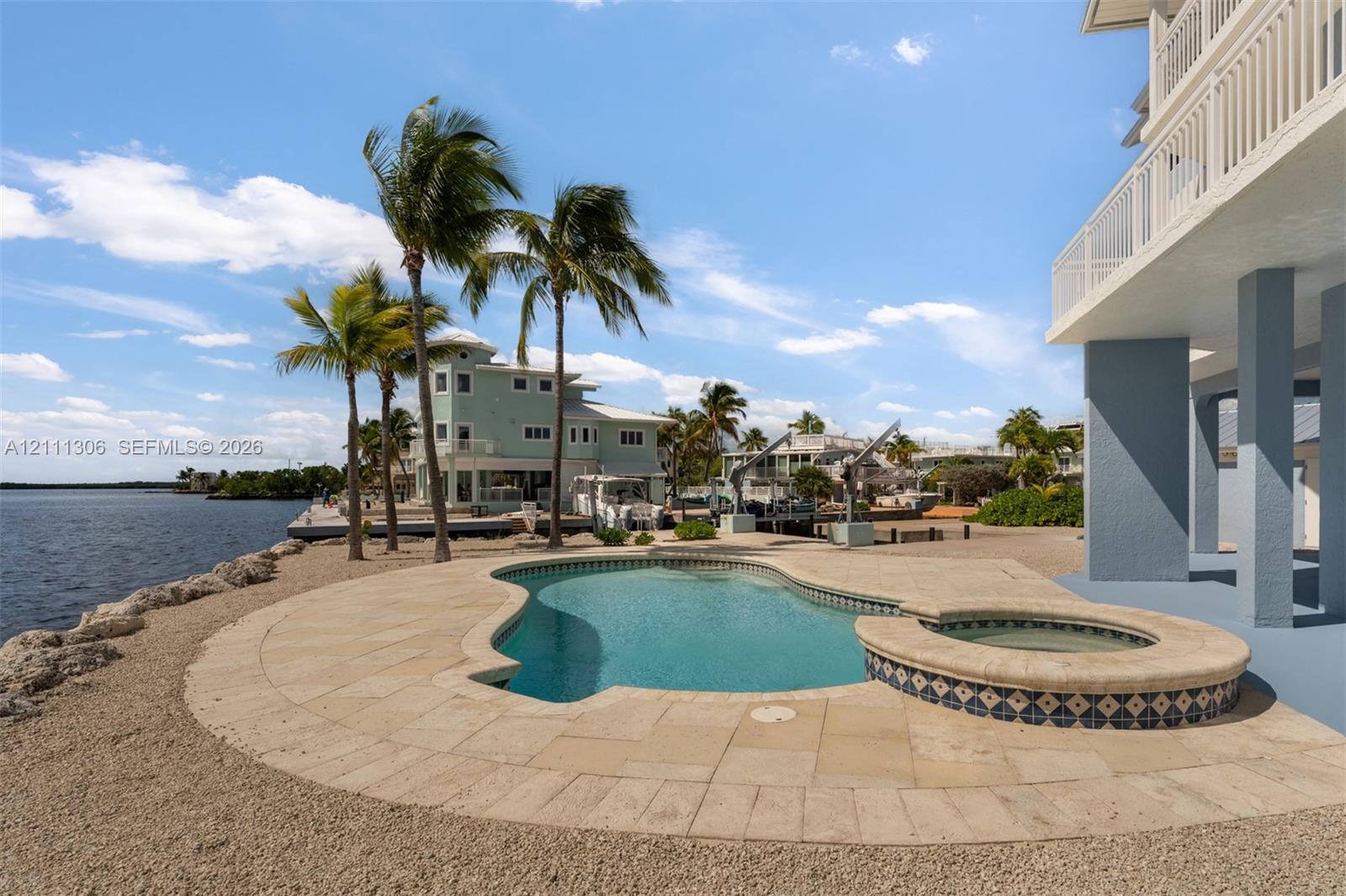 Waterfront pool and spa featuring a stone-paver deck, built-in tiled hot tub, and structural pilings