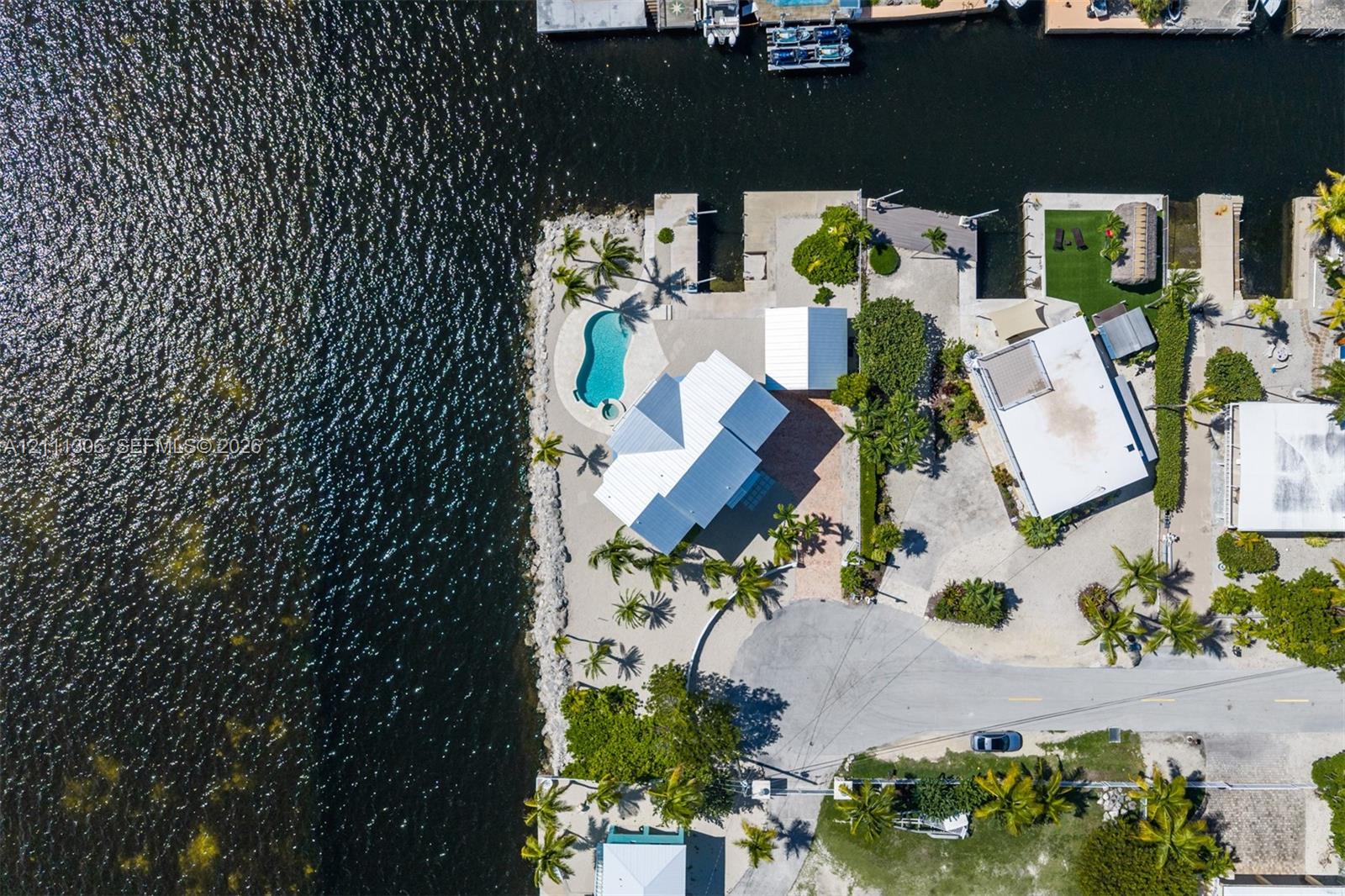 Waterfront property featuring a private boat dock, in-ground swimming pool, paved driveway, and mature palm trees