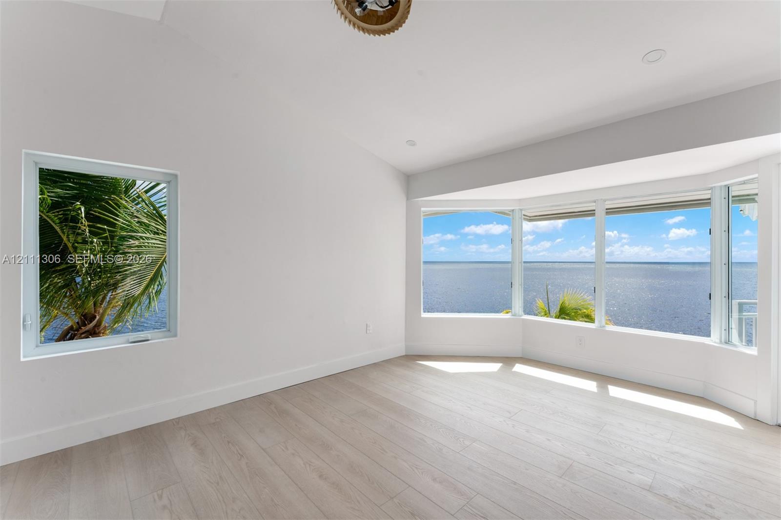 Vaulted ceiling, wood-finish flooring, bay window, and water backdrop