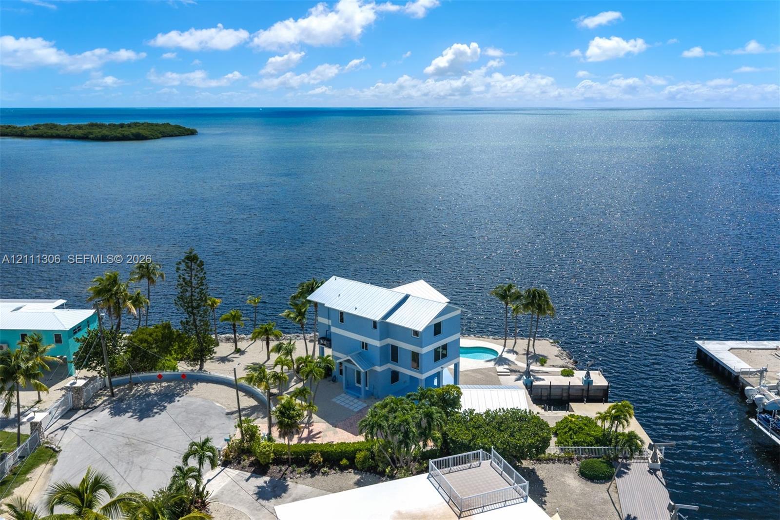 Waterfront multi-story residence featuring a metal roof, an in-ground pool, expansive hardscaping, and established palm trees