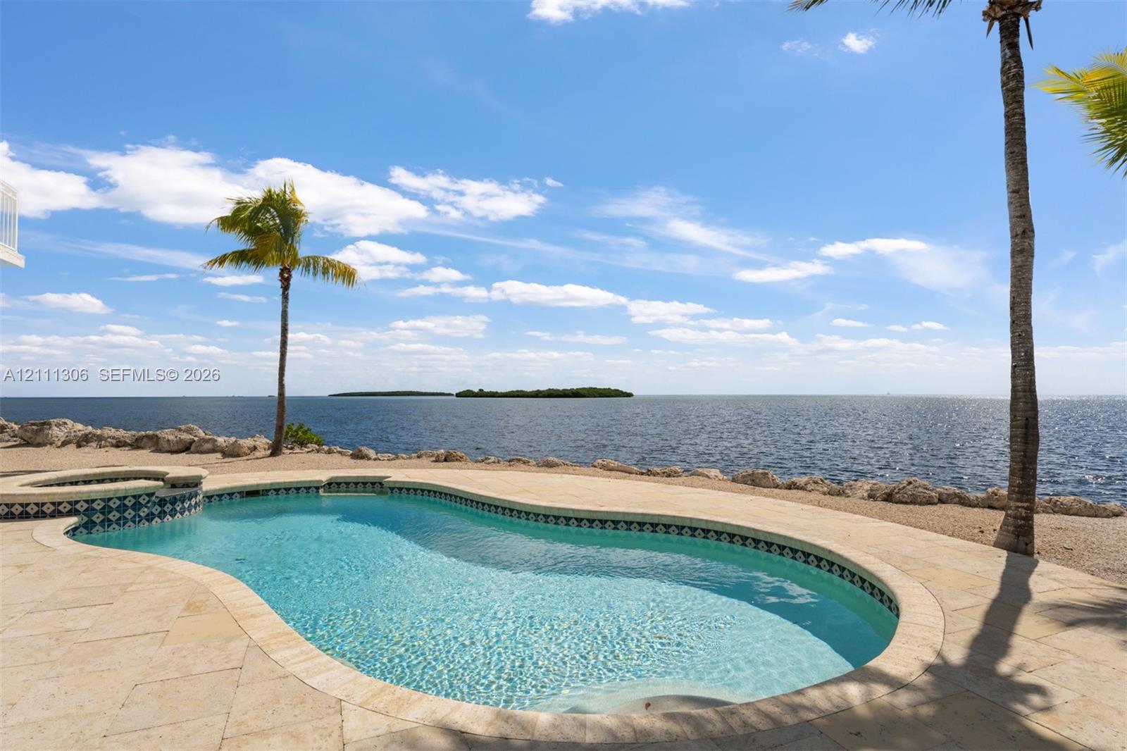 Custom-shaped swimming pool with decorative tile border, integrated spa, and natural stone pool deck bordering an open water shoreline