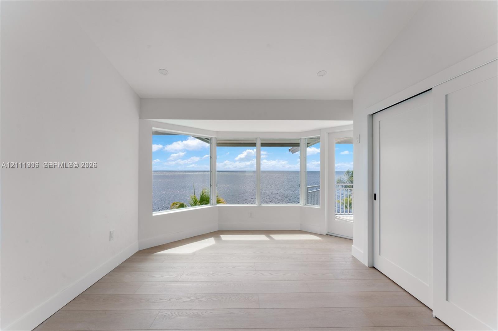 Bay window with expansive water scenery, recessed lighting, wood-finish flooring, and sliding door access to a balcony
