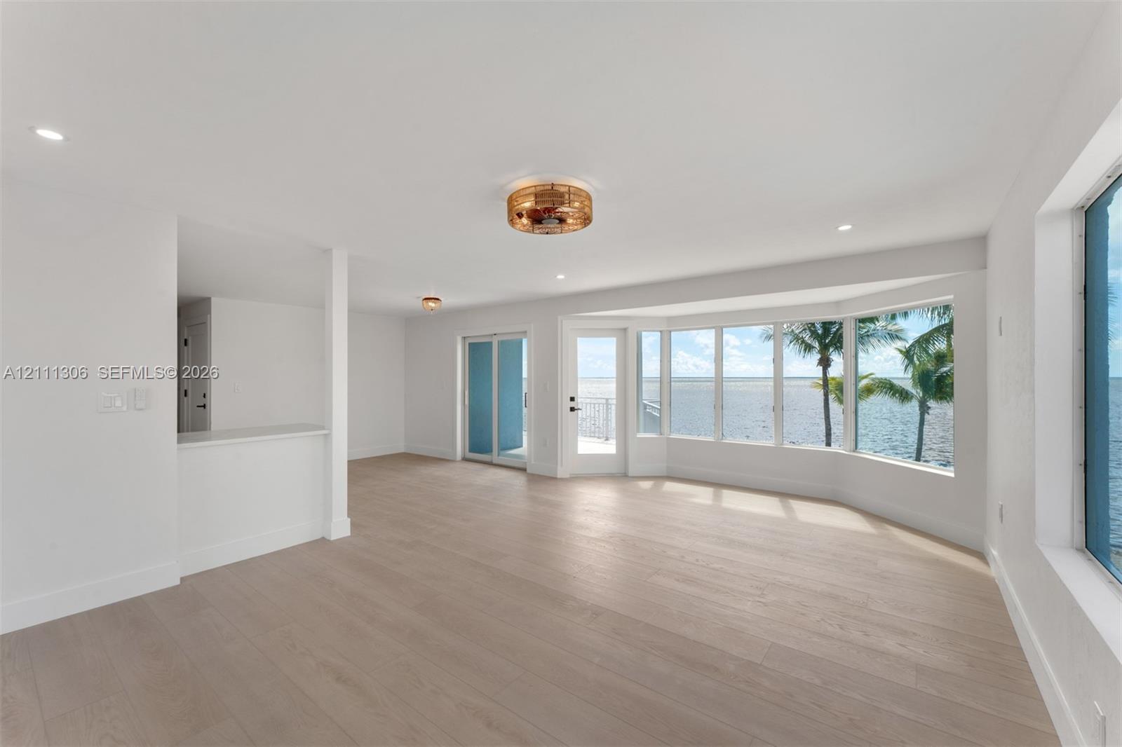 Open-concept interior featuring light-toned wood-finish flooring, a bay window with water frontage, recessed lighting, and a glass-paneled exterior door