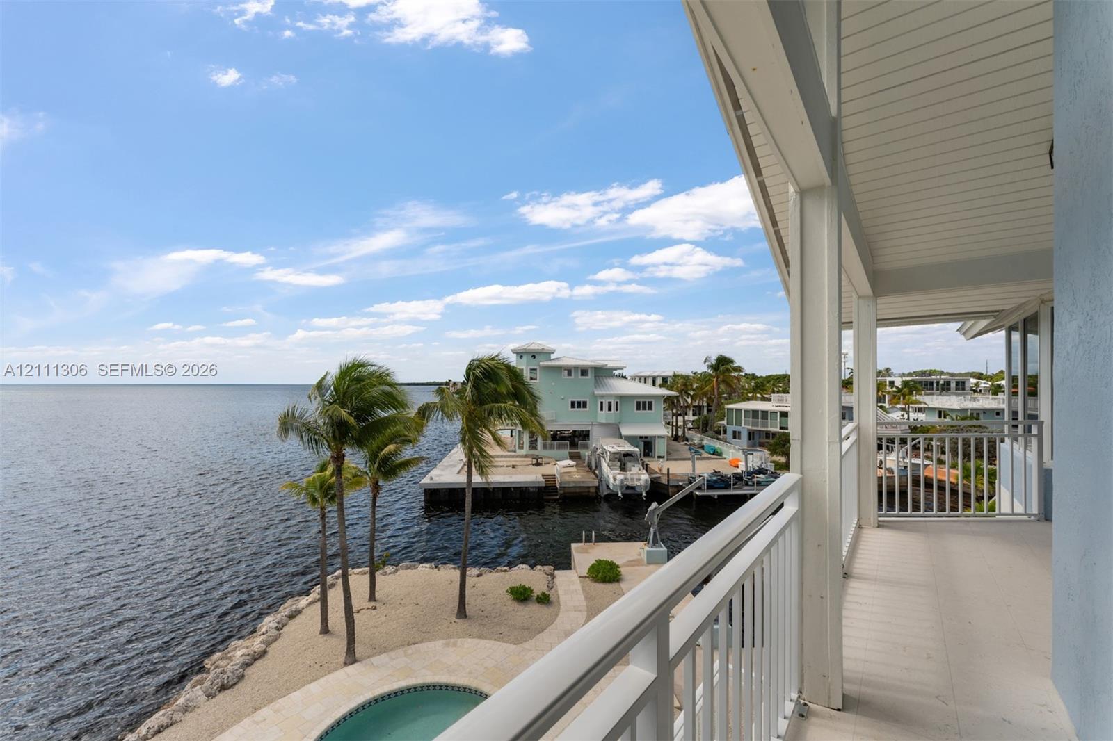Covered balcony featuring white railings, beadboard ceiling, and direct orientation toward the water, including sand beachfront and a pool