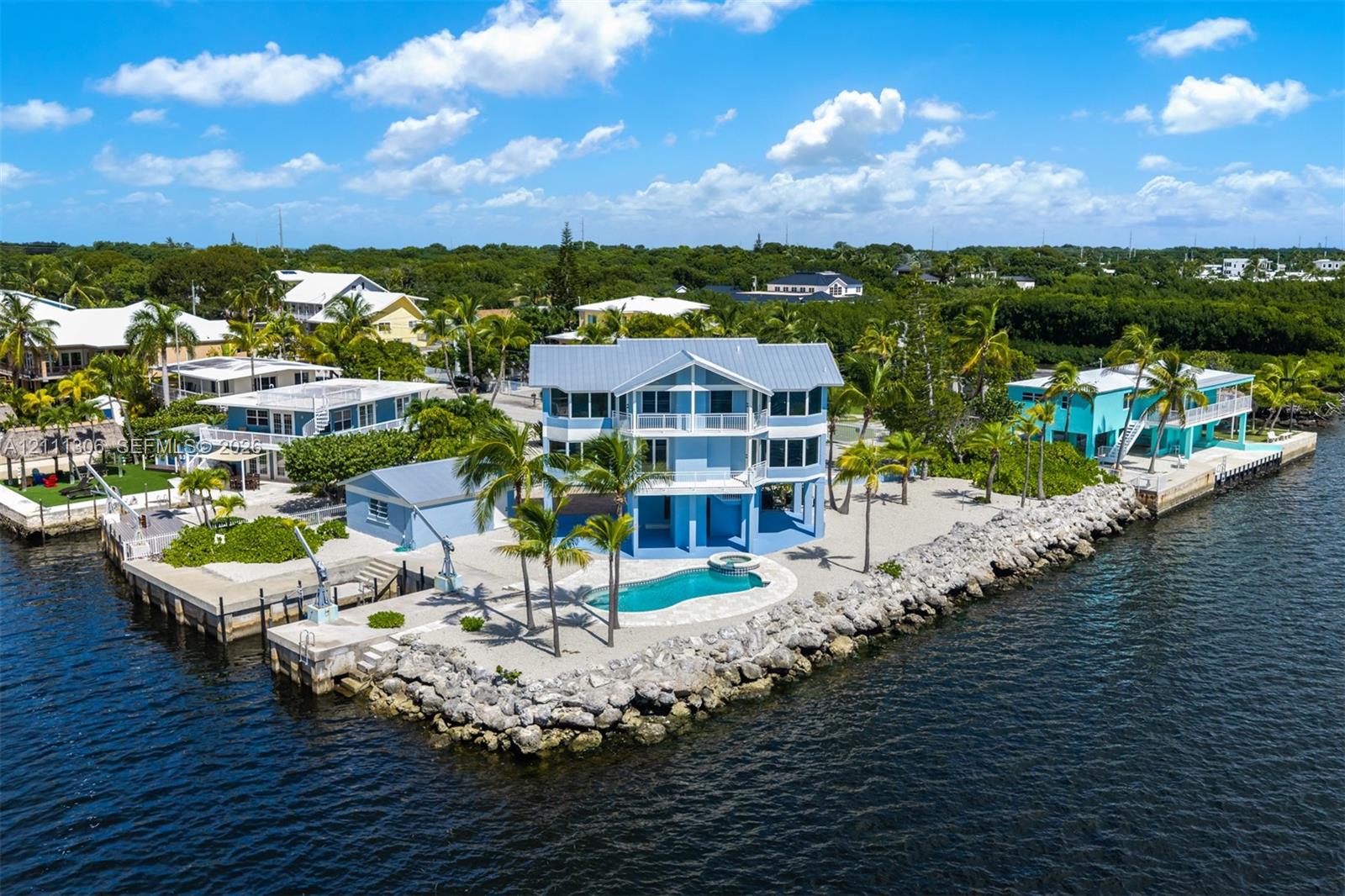 Waterfront property featuring a multi-story residence, private swimming pool, concrete seawall, and integrated boat lift