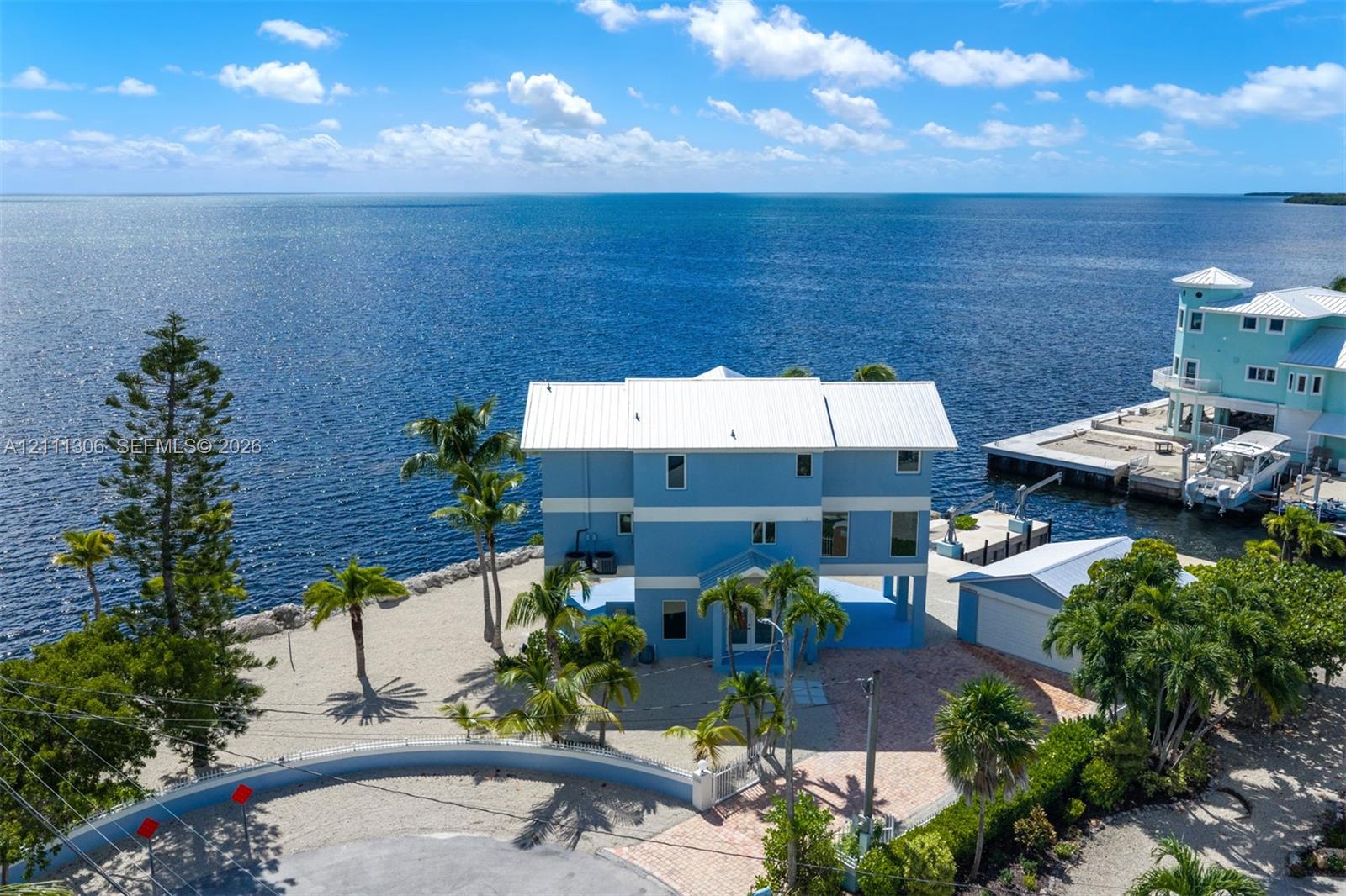 Waterfront residence featuring a metal roof, elevated structural design, private dock, paved driveway, and mature landscaping