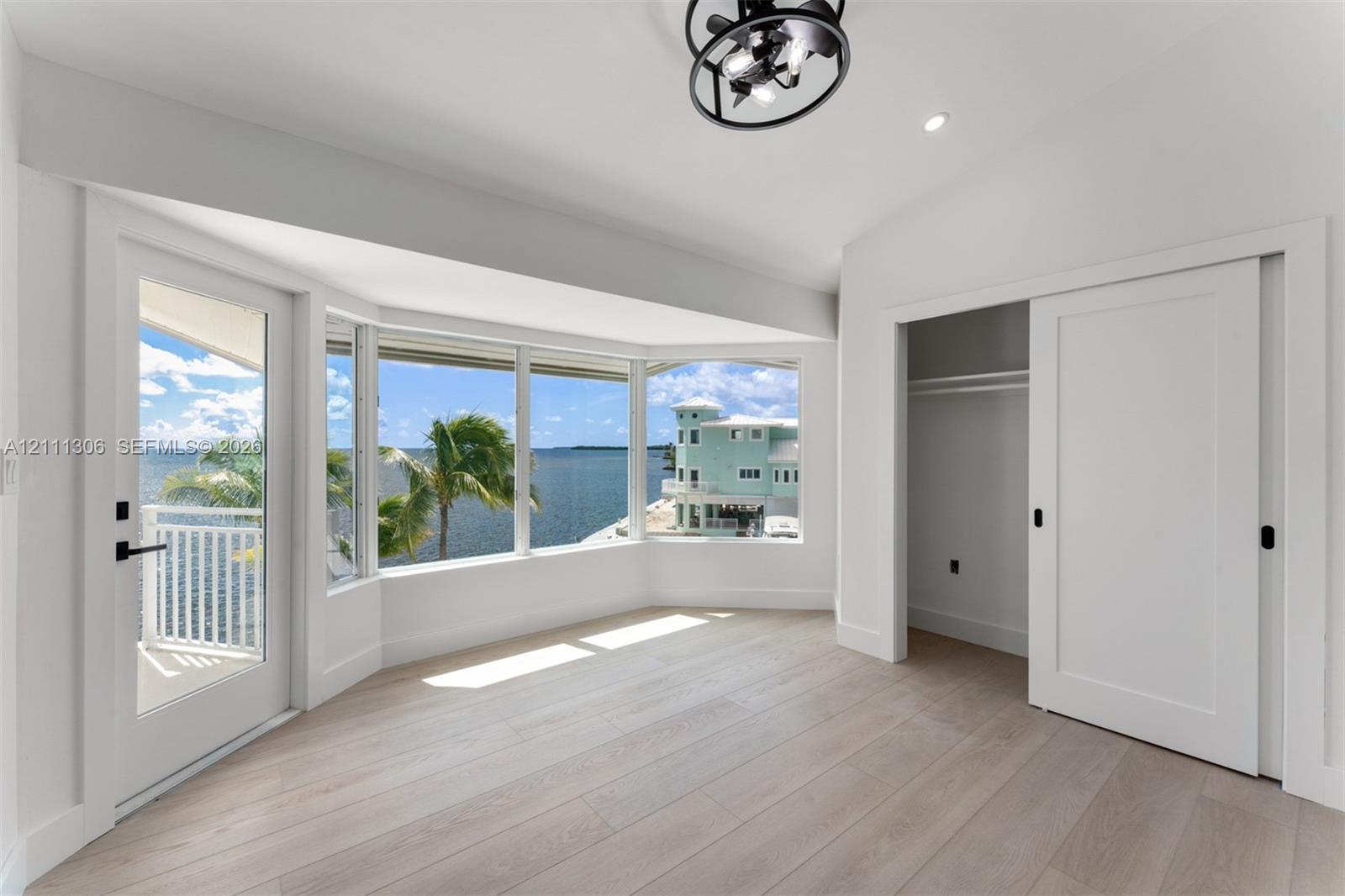 Bay window featuring expansive water scenery, wood-finish flooring, sliding door access to a private balcony, and a modern industrial-style ceiling fixture
