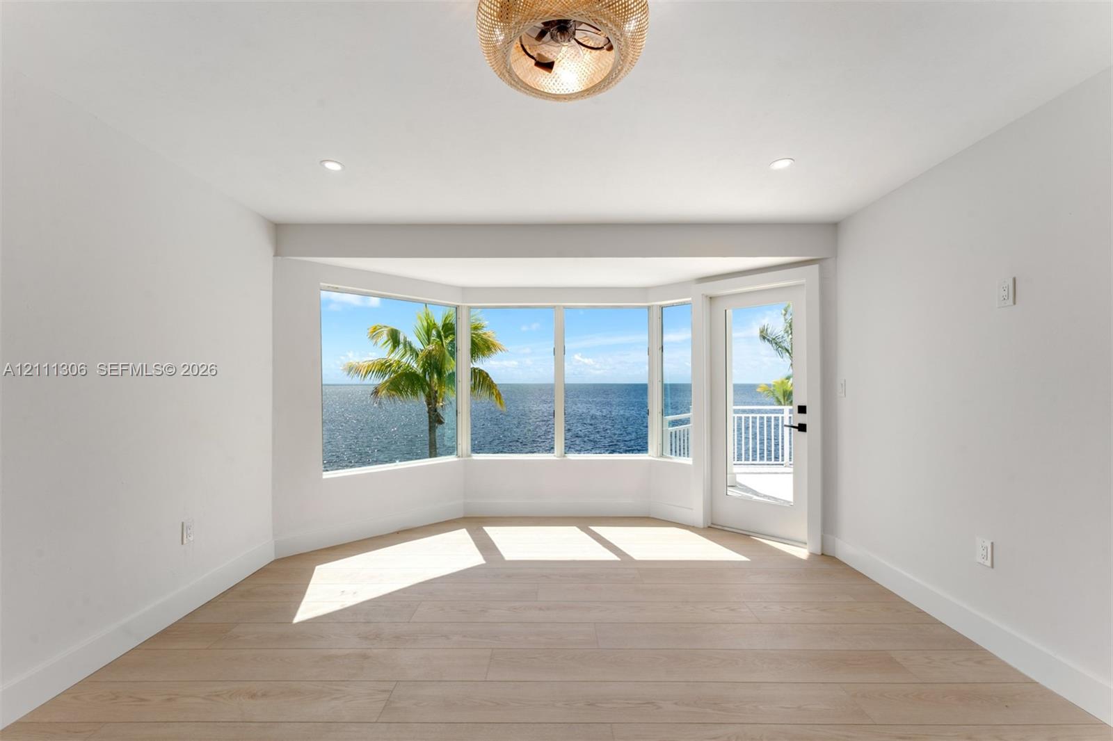 Bay window with water backdrop, wood-finish flooring, recessed lighting, woven-texture ceiling fixture, and glass-paneled exterior door