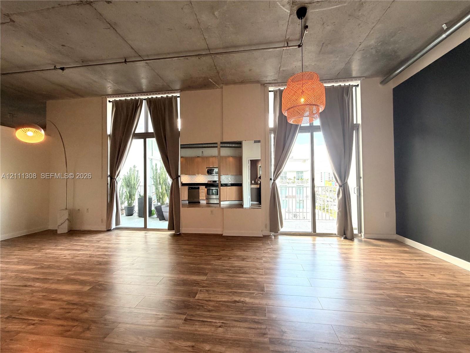 Industrial-style residence featuring an exposed concrete ceiling, wood-finish flooring, dual floor-to-ceiling glass doors, and a built-in cabinetry unit Industrial-style residence featuring an exposed concrete ceiling, wood-finish flooring, dual floor-to-ceiling glass doors, and a built-in cabinetry unit