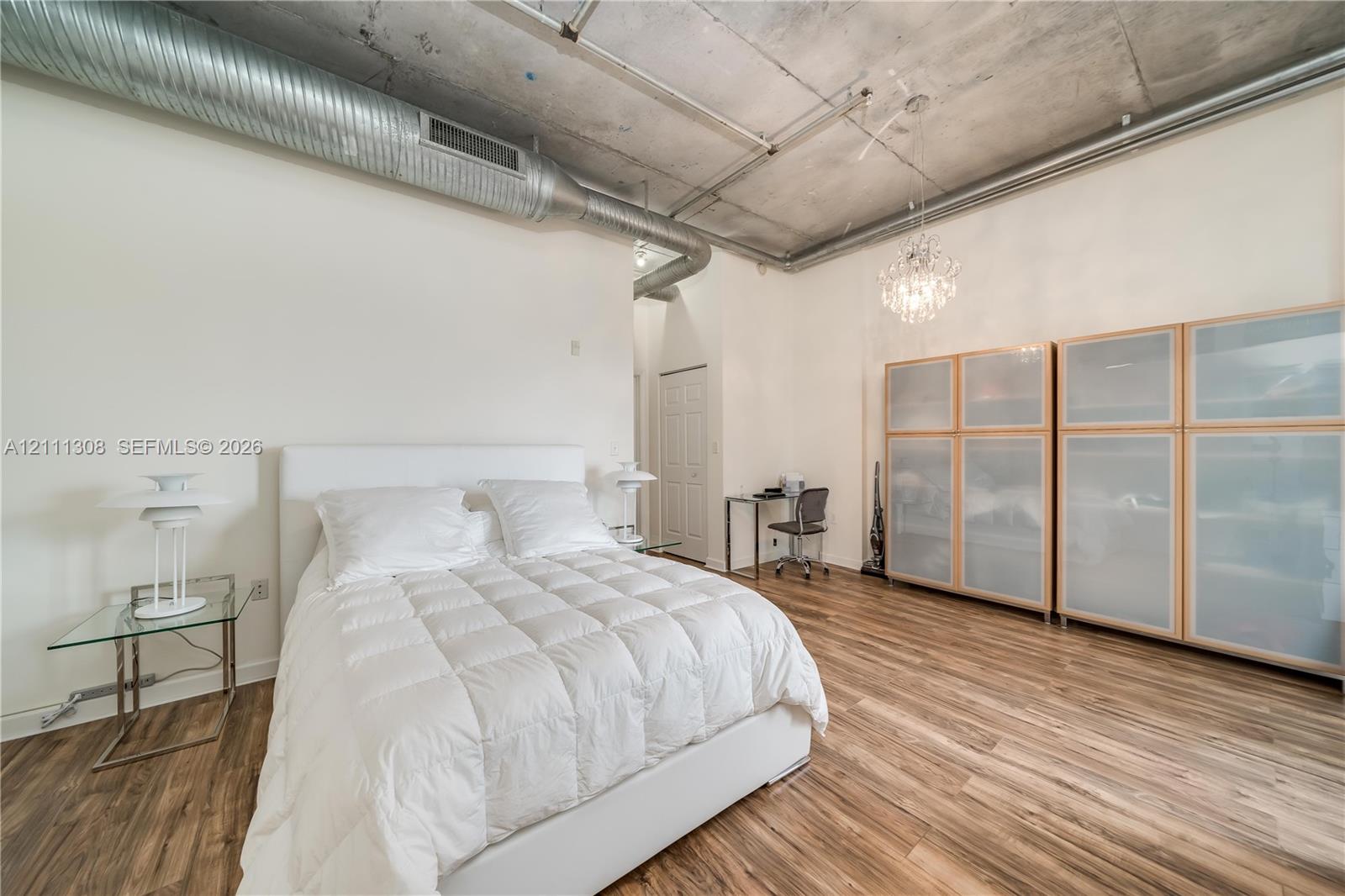 Industrial-style room featuring high concrete ceilings, exposed spiral ductwork, wood-finish flooring, and built-in glass-paneled cabinetry Industrial-style room featuring high concrete ceilings, exposed spiral ductwork, wood-finish flooring, and built-in glass-paneled cabinetry