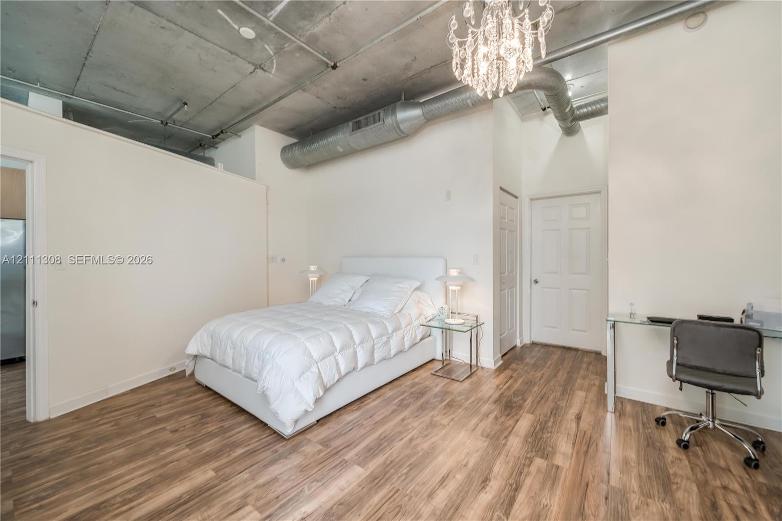 Exposed concrete ceiling with industrial-style ductwork, wood-finish flooring, and a crystal chandelier