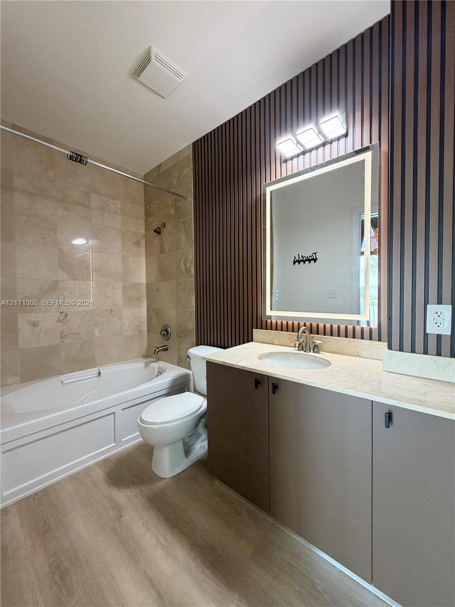 Bathroom featuring a vanity with neutral-toned cabinetry, stone-surface countertop, integrated basin, and an illuminated mirror Bathroom featuring a vanity with neutral-toned cabinetry, stone-surface countertop, integrated basin, and an illuminated mirror