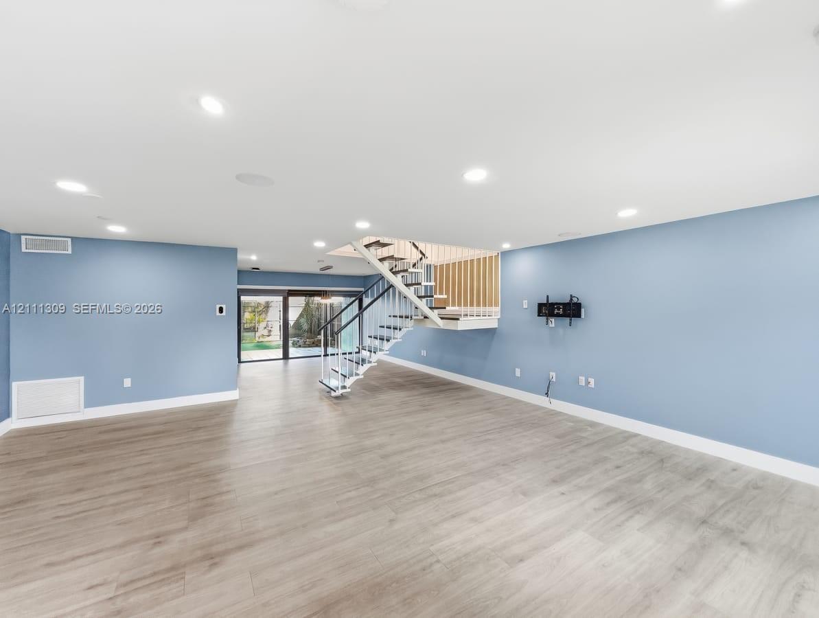 Open interior space featuring wood-finish flooring, recessed lighting, and a staircase with a black metal railing and wooden balusters