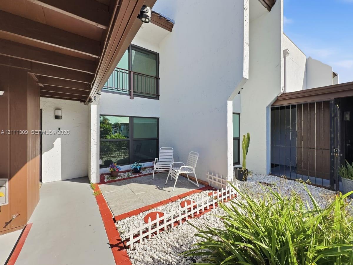 Stucco exterior facade featuring a covered entryway, private stone-paved patio, large windows, and a metal security gate