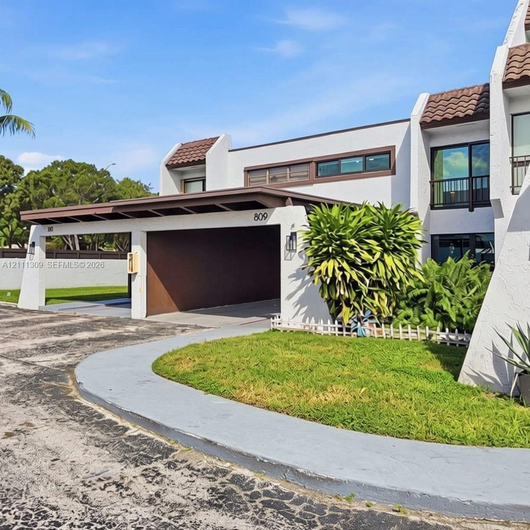 Exterior featuring a stucco facade, covered carport, decorative tile roofing, black-framed windows, and a manicured lawn