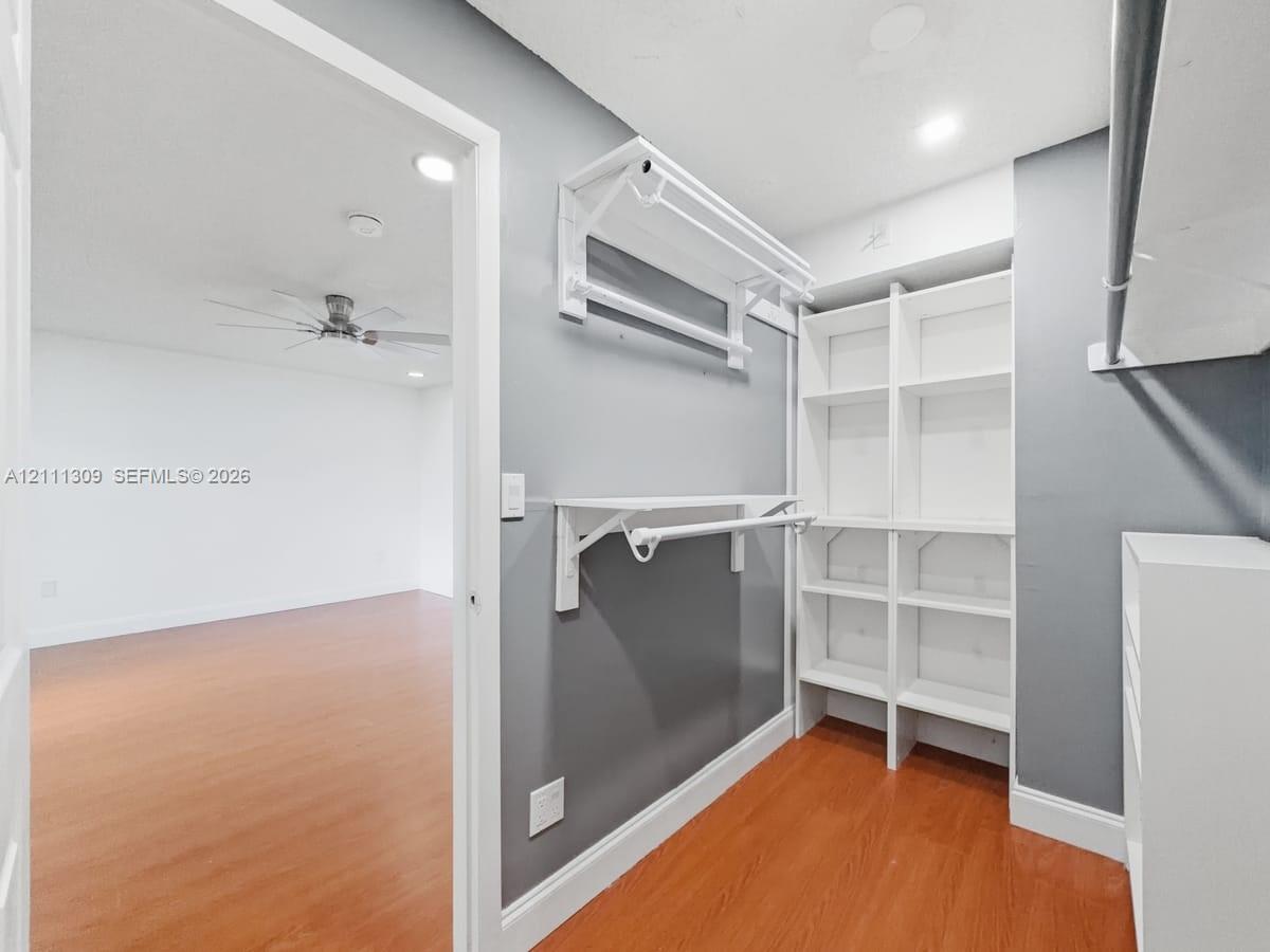 Walk-in closet featuring white built-in shelving, dual-tier hanging rods, and wood-finish flooring