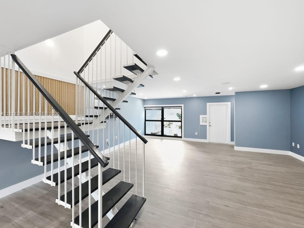 Open-concept interior featuring wood-finish flooring, a contemporary staircase with metal railings, a vertical wood slat accent wall, and recessed ceiling lighting