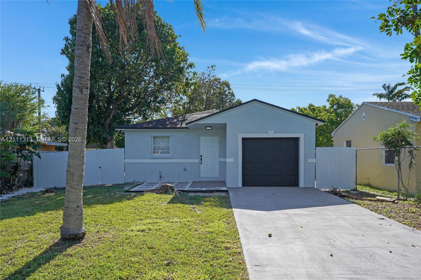 Single-story exterior featuring a painted stucco facade, attached single-car garage, concrete driveway, and solid vinyl perimeter fencing Single-story exterior featuring a painted stucco facade, attached single-car garage, concrete driveway, and solid vinyl perimeter fencing