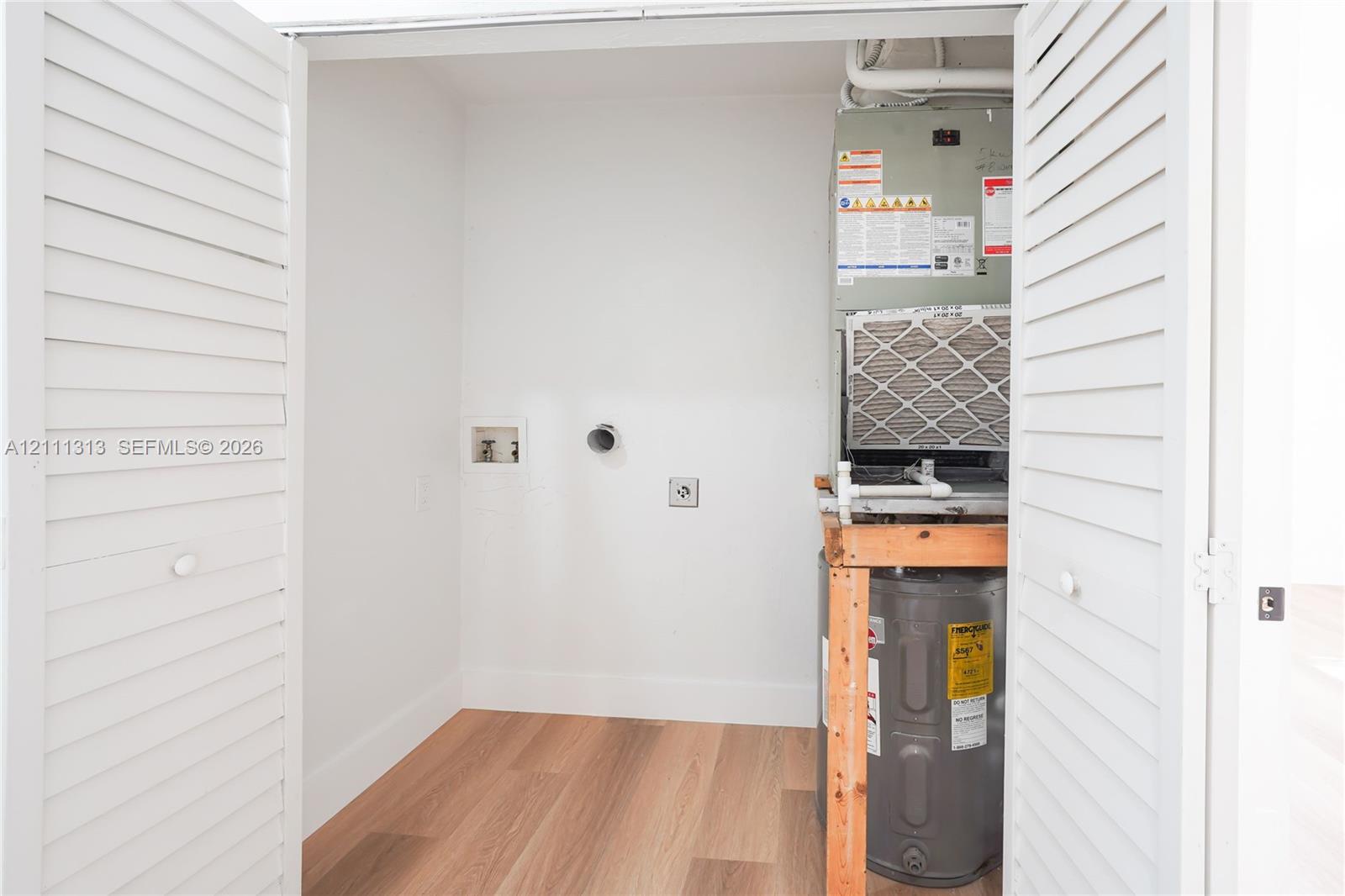 Utility closet featuring wood-finish flooring, white louvered bi-fold doors, water heater, and HVAC system