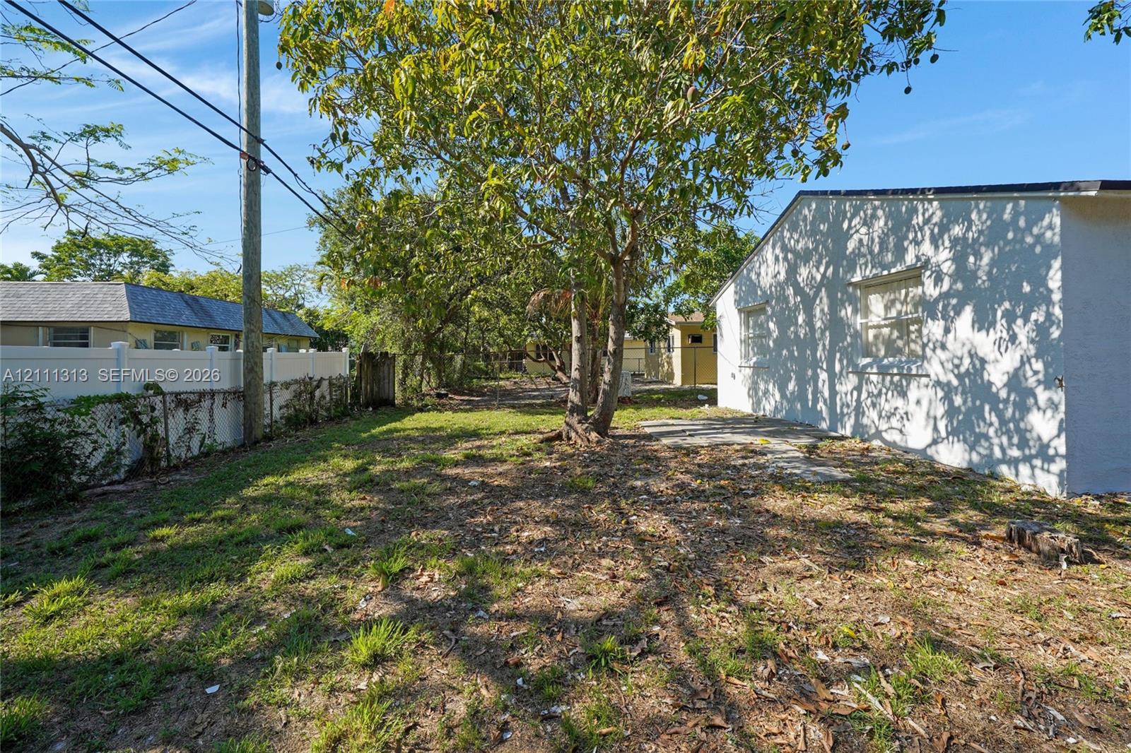 Outdoor space featuring mature trees, a concrete patio, and a white privacy fence