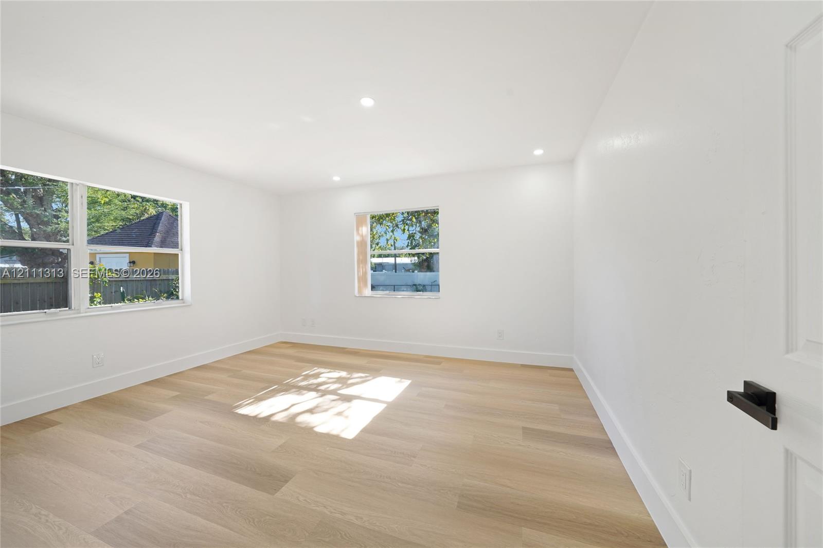 Interior room featuring wood-finish flooring, recessed lighting, white walls, double-pane windows, and a door with matte black hardware