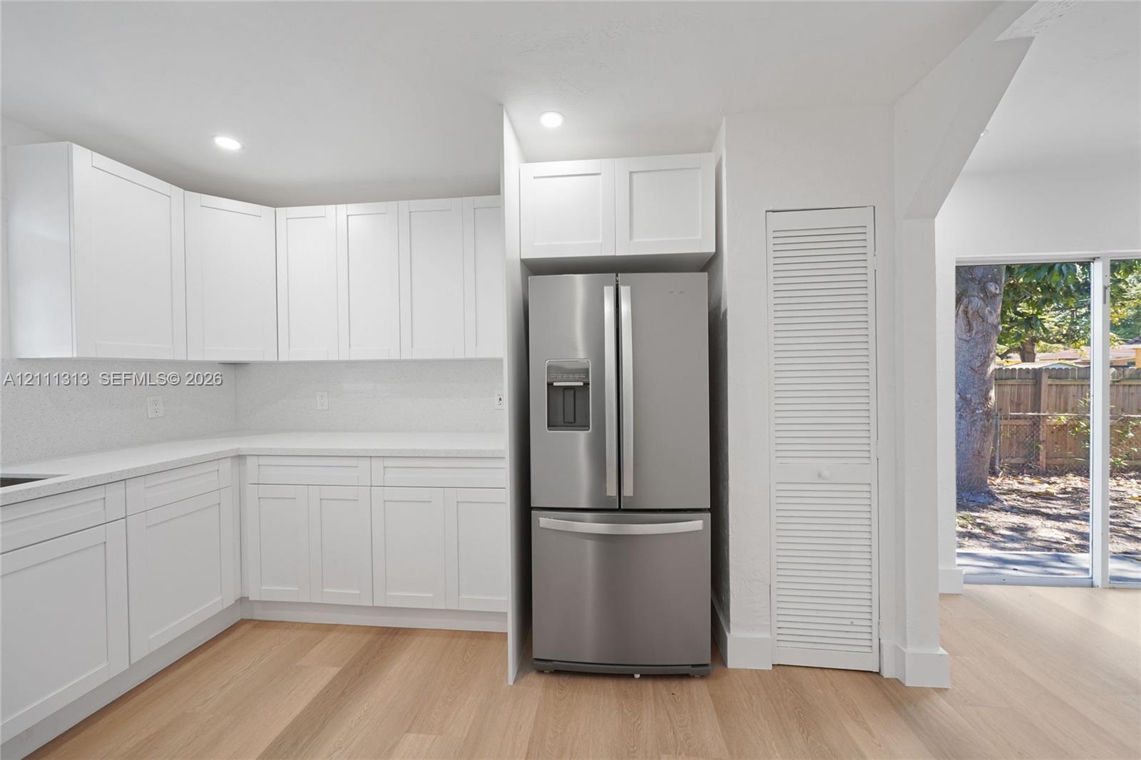 Kitchen featuring white shaker-style cabinetry, solid-surface countertops, stainless steel refrigerator, louvered closet door, and wood-finish flooring