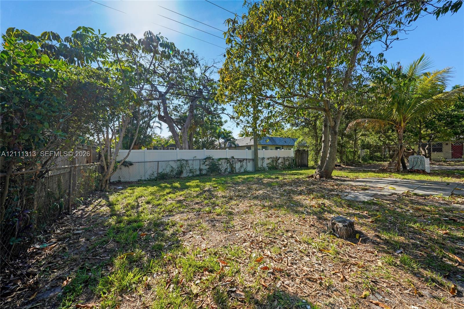 Backyard featuring mature trees, a white vinyl privacy fence, chain-link fencing, and a concrete patio slab