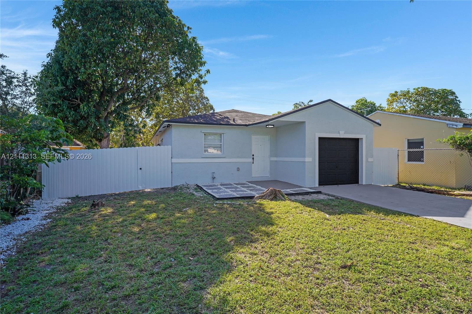 Exterior featuring light-colored stucco siding, a single-car garage with a dark finish, concrete driveway, and white privacy fencing
