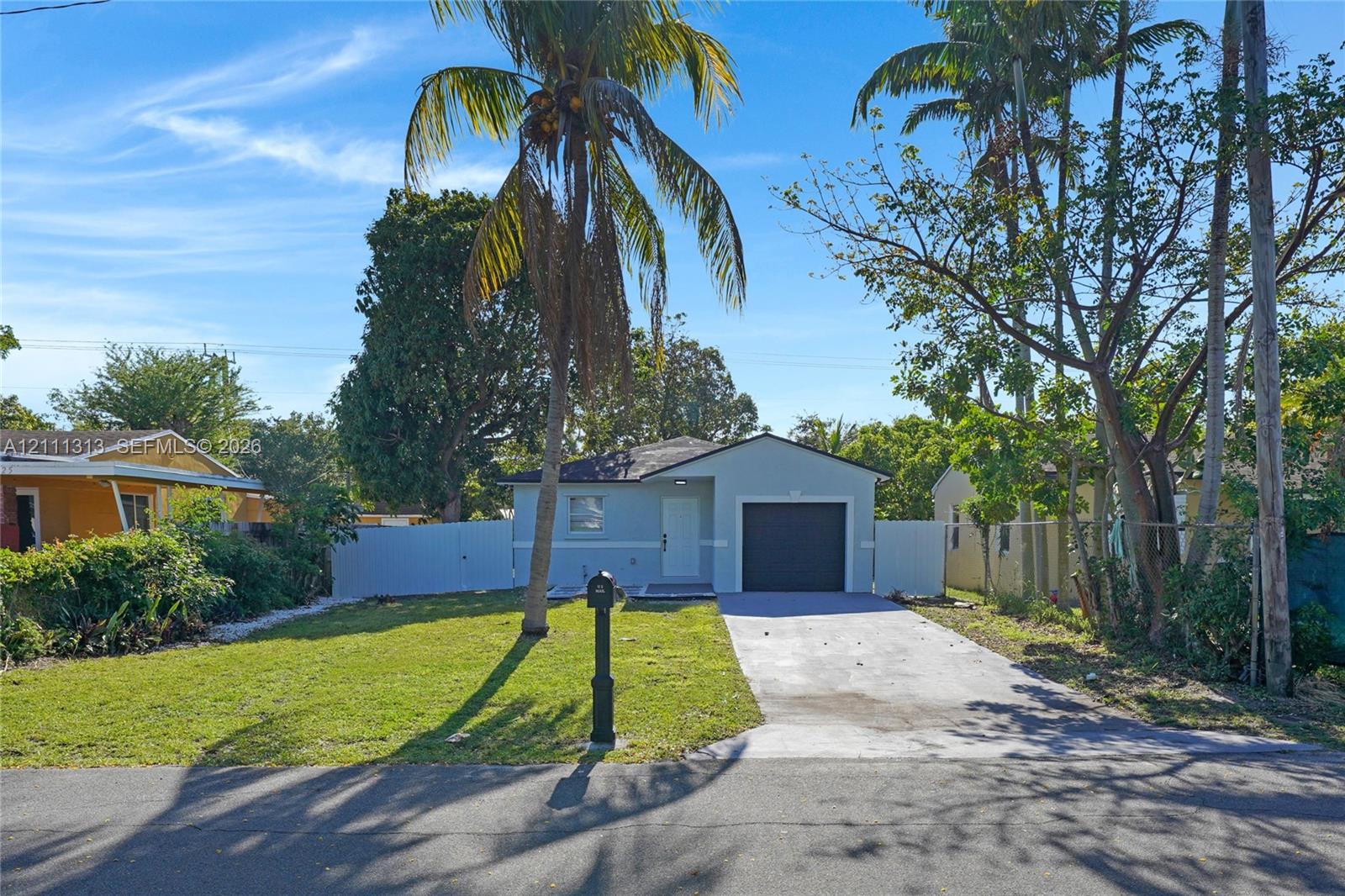 Single-story exterior featuring a light-colored facade, attached single-car garage, concrete driveway, and gated perimeter fencing