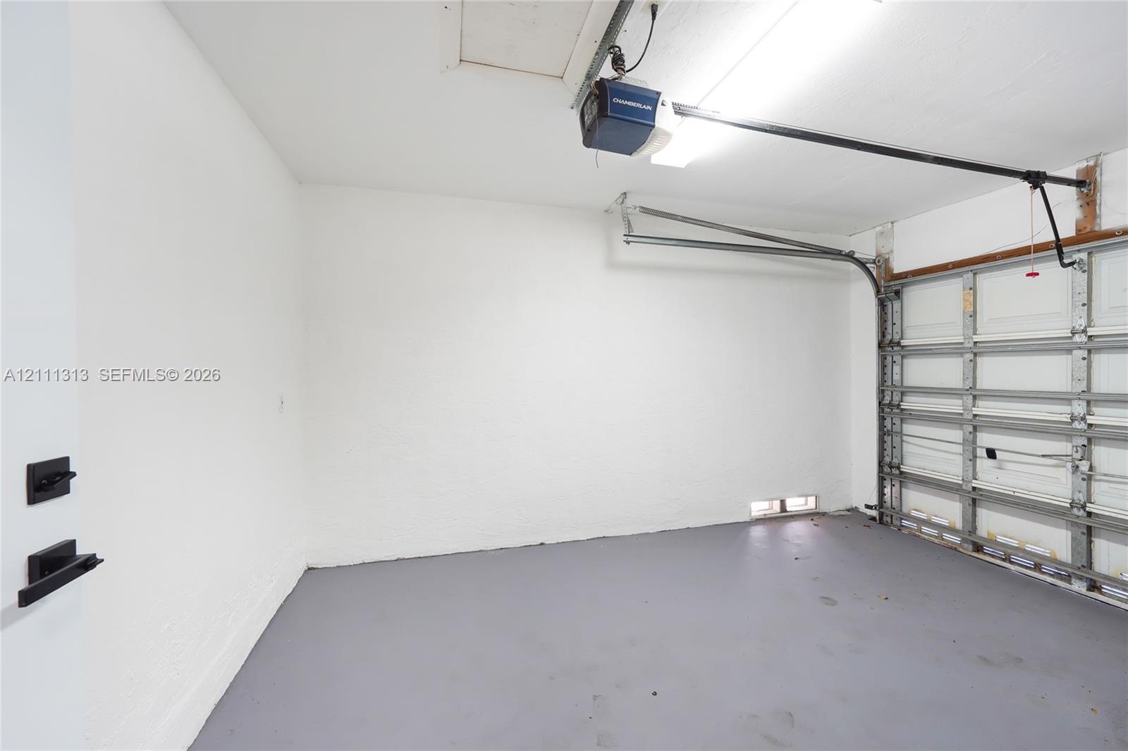 Garage space featuring painted concrete flooring, textured white walls, a motorized door opener, and metal garage door hardware