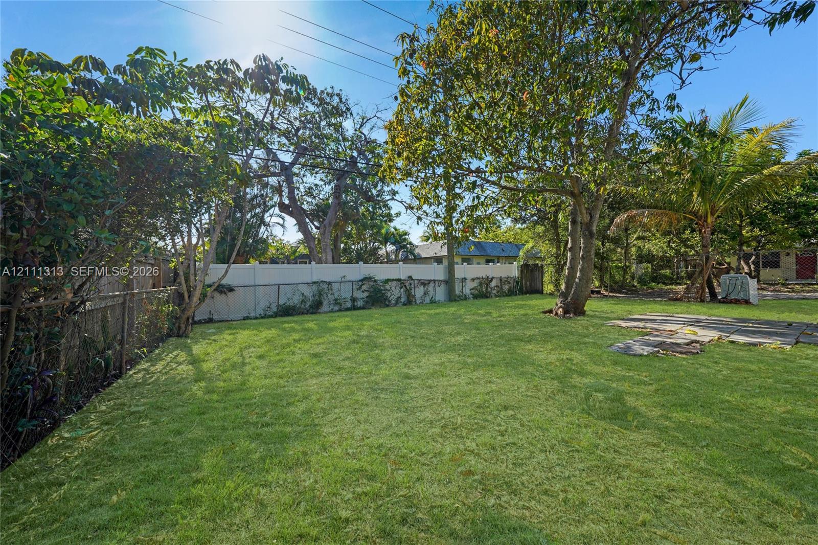 Backyard featuring a grass lawn, mature trees, stone pavers, and a solid privacy fence