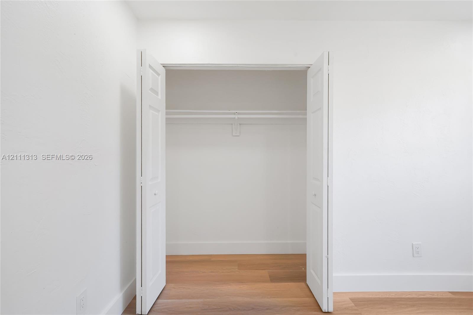 Closet featuring white bi-fold doors, built-in shelving, and wood-finish flooring