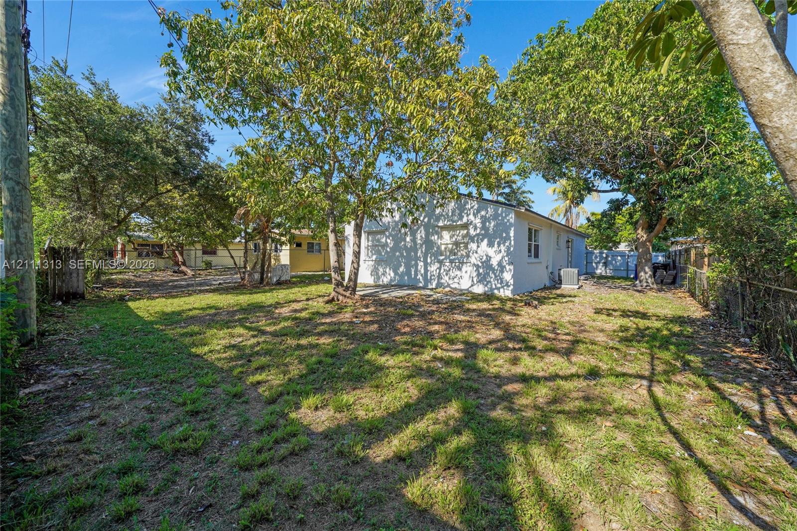 Backyard featuring a grass lawn, mature trees, and chain-link perimeter fencing
