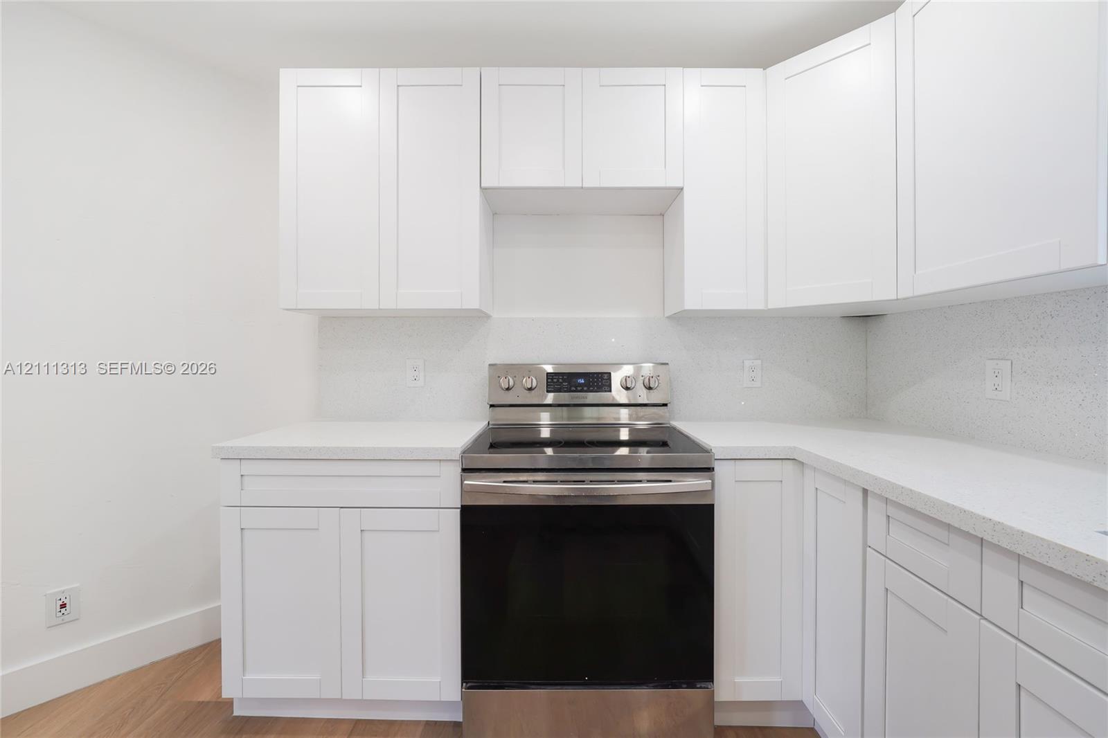 Kitchen featuring white shaker-style cabinetry, white solid-surface countertops, coordinating backsplash, and a stainless steel freestanding range with glass cooktop, finished with wood-finish flooring