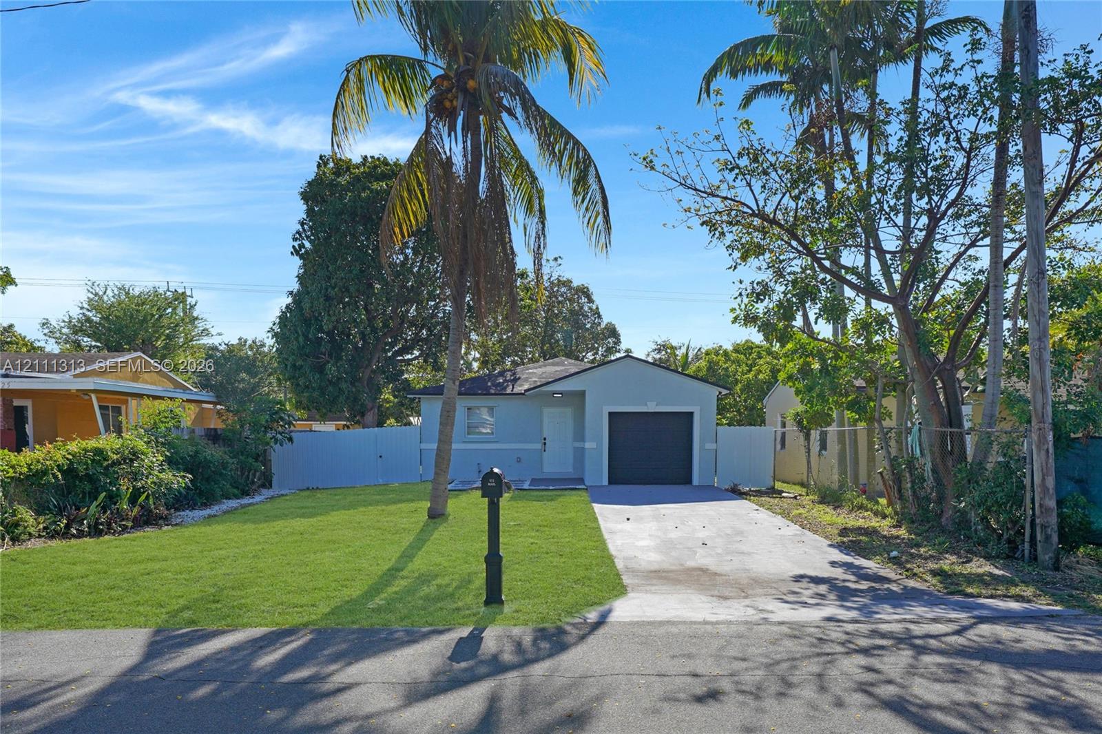 Single-story exterior featuring a concrete driveway, attached one-car garage, manicured lawn, and perimeter privacy fencing