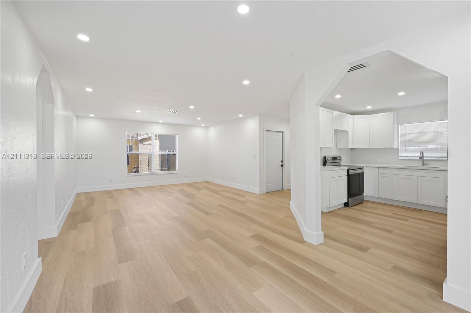 Open-concept living space featuring wood-finish flooring, recessed lighting, white cabinetry, integrated stainless steel appliances, and quartz countertops