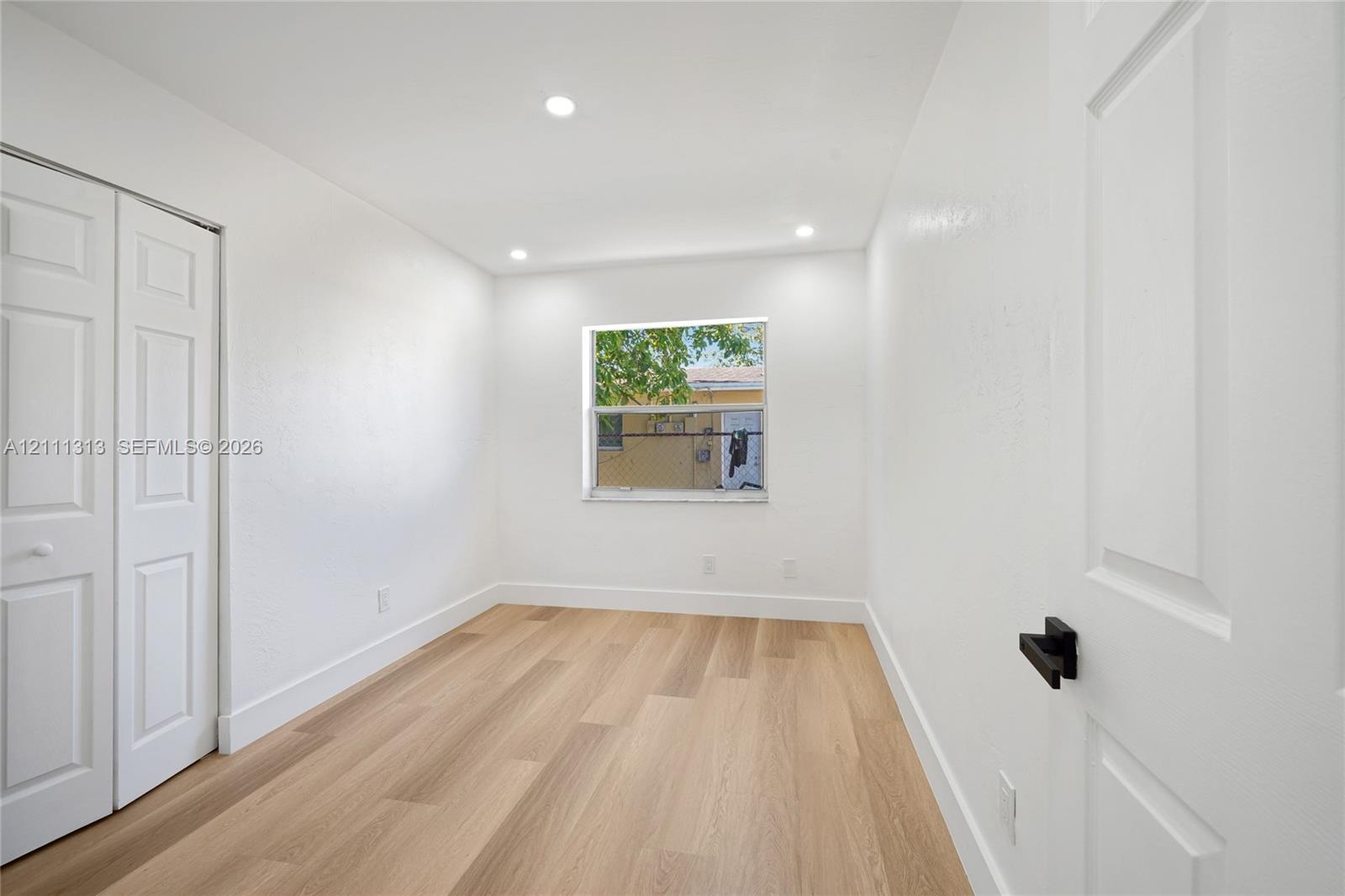 Interior room featuring wood-finish flooring, recessed lighting, white panel doors, and a window with a neutral finish